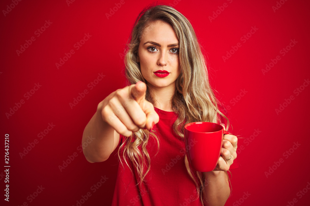 Young beautiful woman drinking a cup of cooffe over red isolated background pointing with finger to the camera and to you, hand sign, positive and confident gesture from the front Young beautiful woman drinking a cup of cooffe over red isolated background pointing with finger to the camera and to you, hand sign, positive and confident gesture from the front
