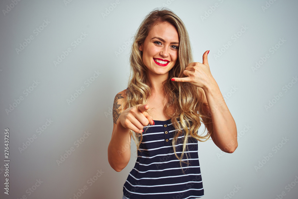 Young beautiful woman wearing stripes t-shirt standing over white isolated background smiling doing talking on the telephone gesture and pointing to you. Call me. Young beautiful woman wearing stripes t-shirt standing over white isolated background smiling doing talking on the telephone gesture and pointing to you. Call me.