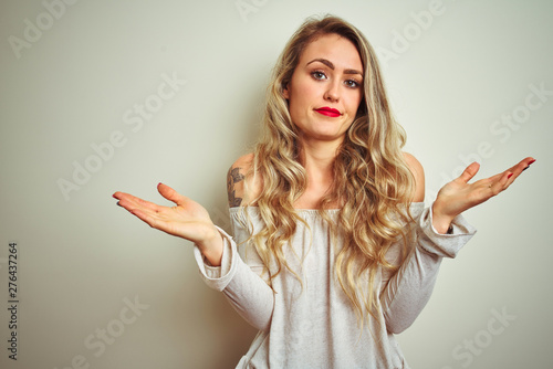 Young beautiful woman standing over white isolated background clueless and confused expression with arms and hands raised. Doubt concept.