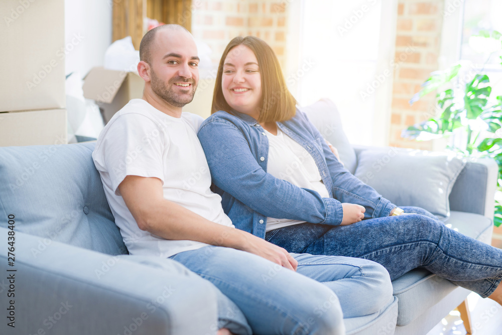 Young couple in love relaxing and hugging sitting on the sofa at new home, smiling very happy for moving to a new apartment