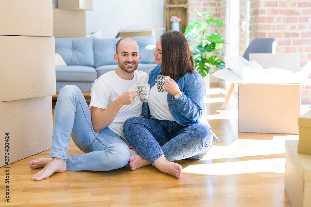 Young couple sitting on the floor of new house arround cardboard boxing, relaxing from moving drinking a cup of coffee smiling very happy Young couple sitting on the floor of new house arround cardboard boxing, relaxing from moving drinking a cup of coffee smiling very happy