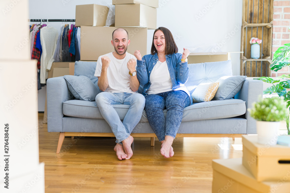 Young couple sitting on the sofa arround cardboard boxes moving to a new house celebrating surprised and amazed for success with arms raised and open eyes. Winner concept. Young couple sitting on the sofa arround cardboard boxes moving to a new house celebrating surprised and amazed for success with arms raised and open eyes. Winner concept.