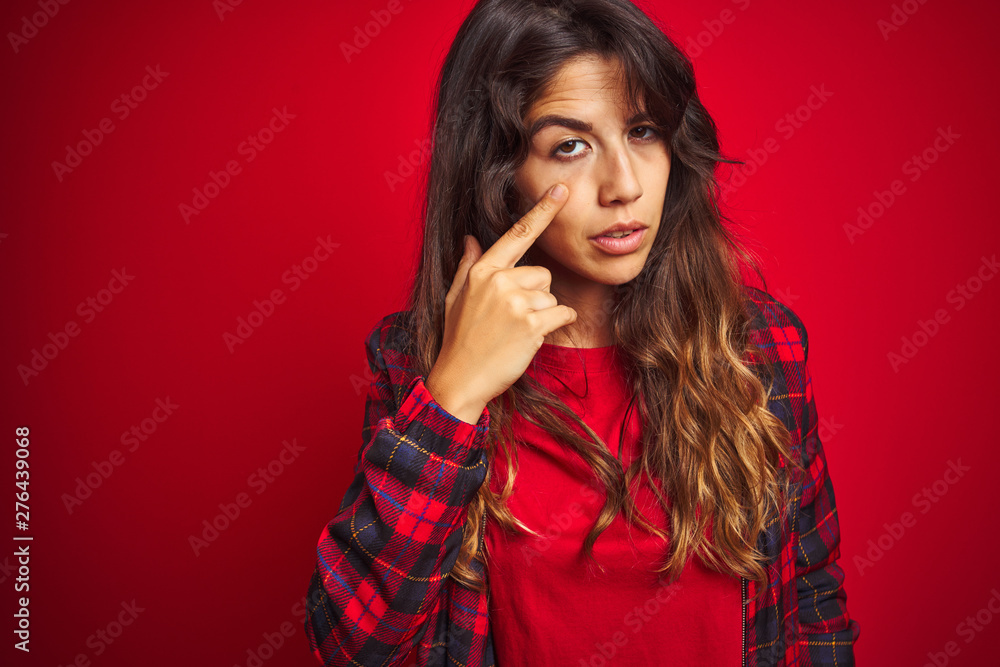 Young beautiful woman wearing casual jacket standing over red isolated background Looking fascinated with disbelief, surprise and amazed expression with hands on chin Young beautiful woman wearing casual jacket standing over red isolated background Looking fascinated with disbelief, surprise and amazed expression with hands on chin