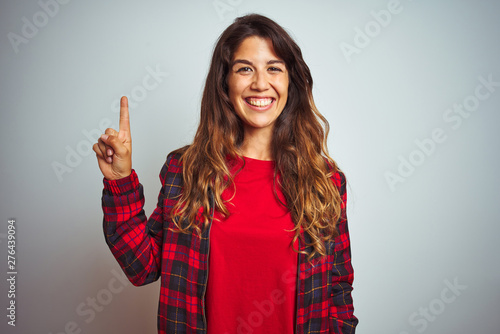 Young beautiful woman wearing red t-shirt and jacket standing over white isolated background showing and pointing up with finger number one while smiling confident and happy.