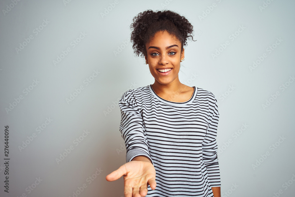 Fototapeta premium African american woman wearing navy striped t-shirt standing over isolated white background smiling cheerful offering palm hand giving assistance and acceptance.