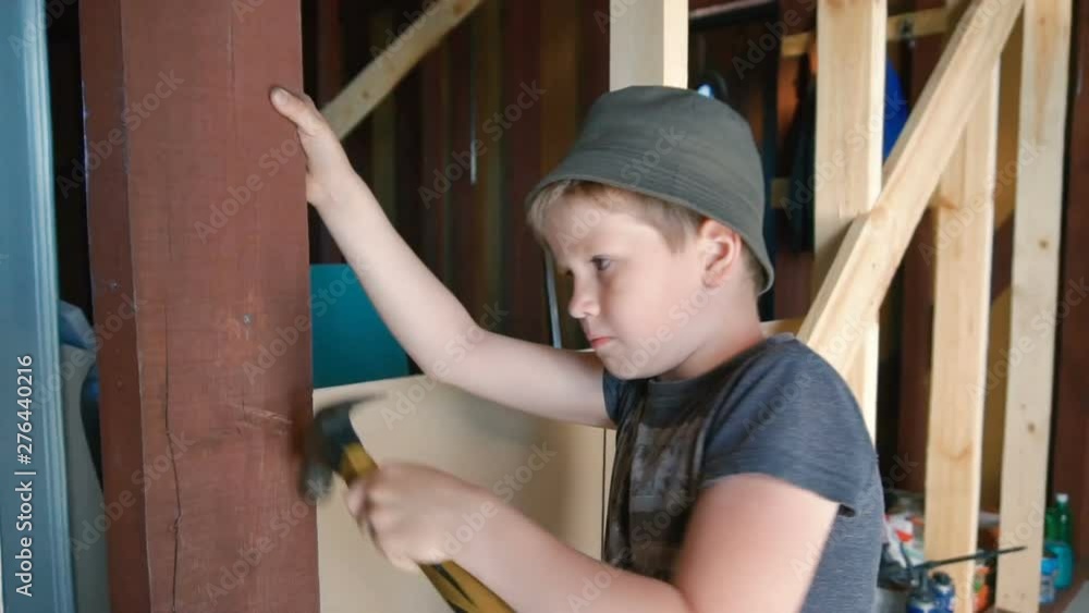 A boy is hammering a nail into a wooden block. Small stature. Summer time of the year. Home construction. Indoors. A boy is hammering a nail into a wooden block. Small stature. Summer time of the year. Home construction. Indoors.