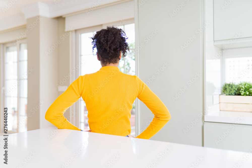 Beautiful african american woman with afro hair wearing a casual yellow sweater standing backwards looking away with arms on body Beautiful african american woman with afro hair wearing a casual yellow sweater standing backwards looking away with arms on body