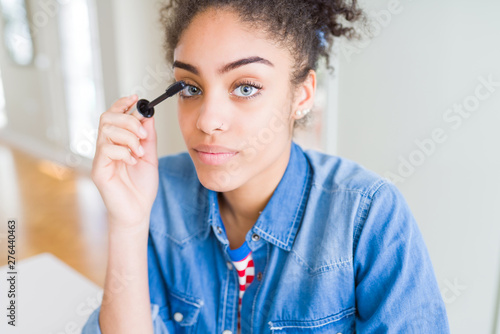 Young african american girl applying eyelashes mascara with a confident expression on smart face thinking serious