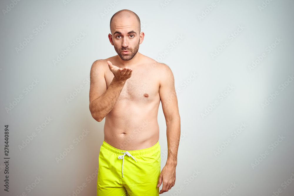 Fototapeta premium Young shirtless man on vacation wearing yellow swimwear over isolated background looking at the camera blowing a kiss with hand on air being lovely and sexy. Love expression.