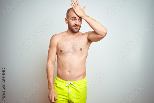 Young shirtless man on vacation wearing yellow swimwear over isolated background surprised with hand on head for mistake  remember error. Forgot  bad memory concept.