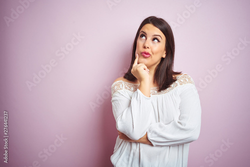 Young beautiful brunette woman over pink isolated background with hand on chin thinking about question, pensive expression. Smiling with thoughtful face. Doubt concept.