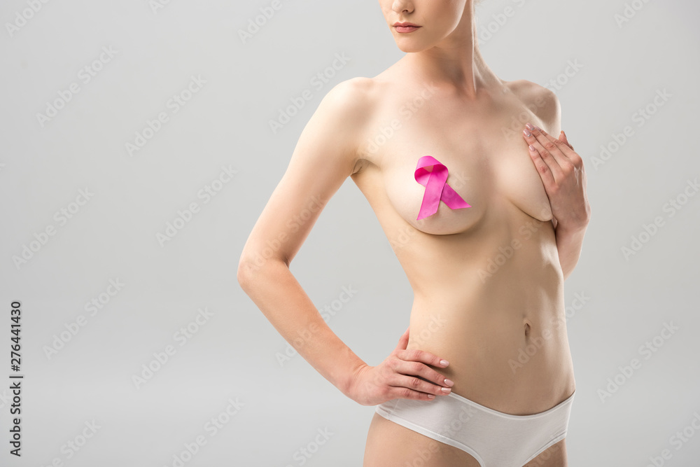 partial view of topless young woman in panties with pink ribbon covering breast isolated on grey