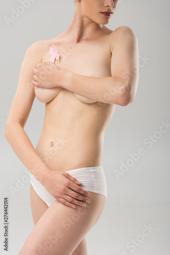 partial view of topless young woman in white panties with pink ribbon covering breast isolated on grey © LIGHTFIELD STUDIOS