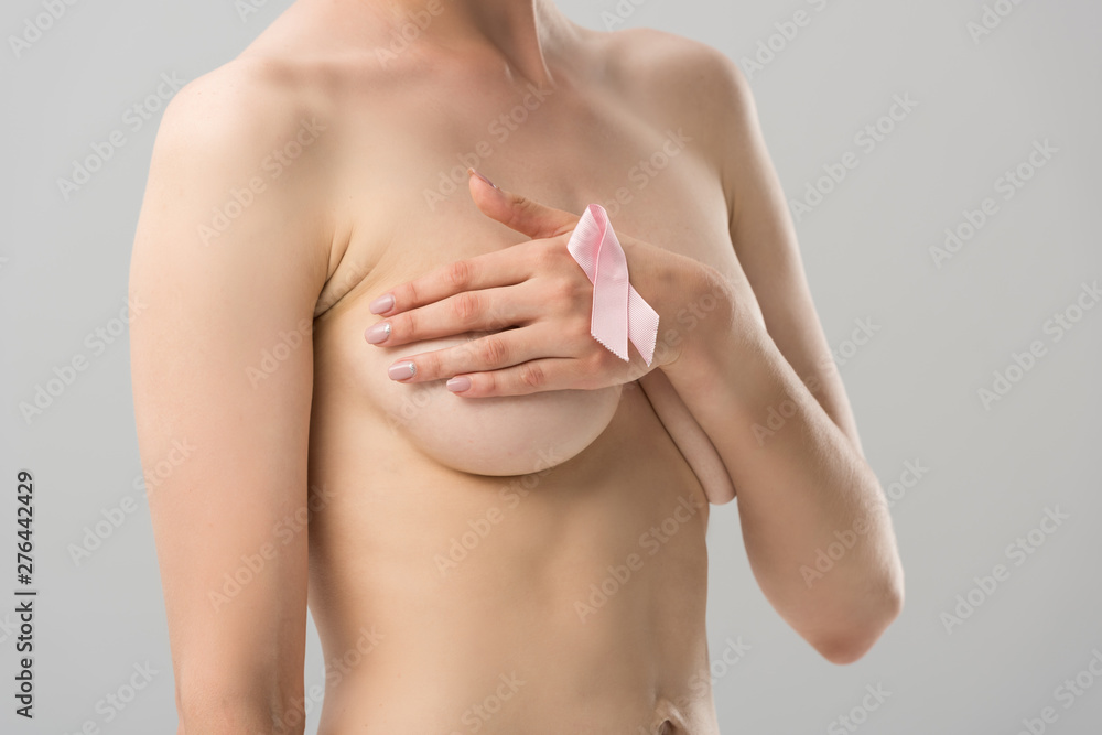 Fototapeta premium partial view of topless young woman with pink ribbon covering breast isolated on grey