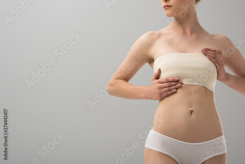 cropped view of woman in panties with breast bandage isolated on grey photo