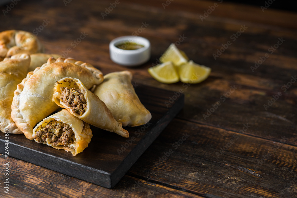 Traditional baked Argentine empanadas savoury pastries with meat beef stuffing against wooden background - obrazy, fototapety, plakaty 