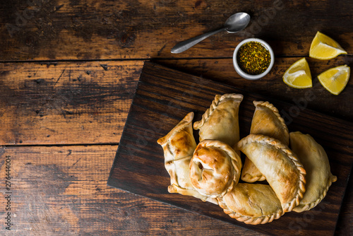 Traditional baked Argentine empanadas savoury pastries with meat beef stuffing against wooden background