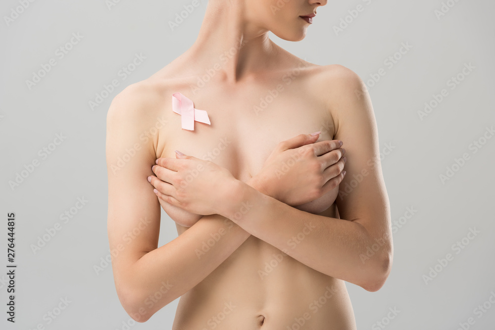 partial view of topless young woman with pink ribbon covering breast isolated on grey partial view of topless young woman with pink ribbon covering breast isolated on grey