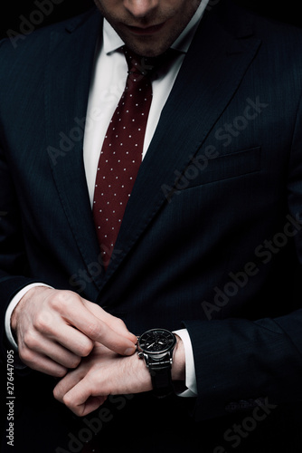 cropped view of businessman checking time on watch isolated on black