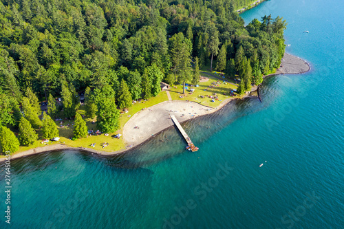 Aerial photo of Cultus Lake in Chilliwack, B.C. while people are enjoying the summer activities at the lakeshore and doing barbeque in the woods by the lake