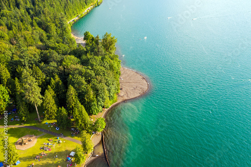 Aerial photo of Cultus Lake in Chilliwack, B.C. while people are enjoying the summer activities at the lakeshore and doing barbeque in the woods by the lake