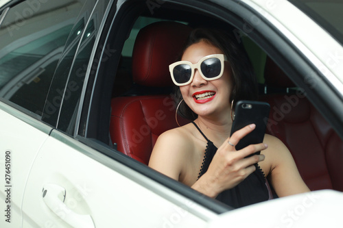 Beautiful woman is using a smart phone and smiling while sitting iin the car .