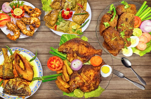 Indian fish food dishes on display comprising of deep fried pomfret fish with  hilsa fish oil curry and deep fried crispy prawn served with salad on wooden background photo
