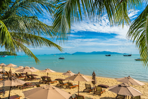 Beautiful tropical beach sea and ocean with coconut palm tree and umbrella and chair on blue sky and white cloud