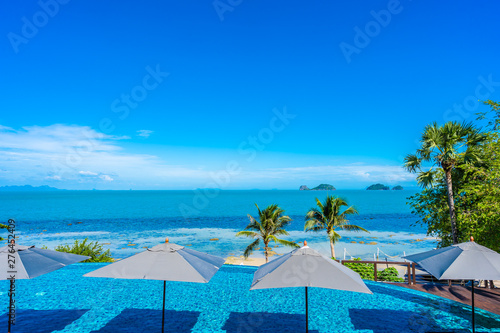 Beautiful luxury outdoor swimming pool in hotel resort with sea ocean around coconut palm tree and white cloud on blue sky © siraphol