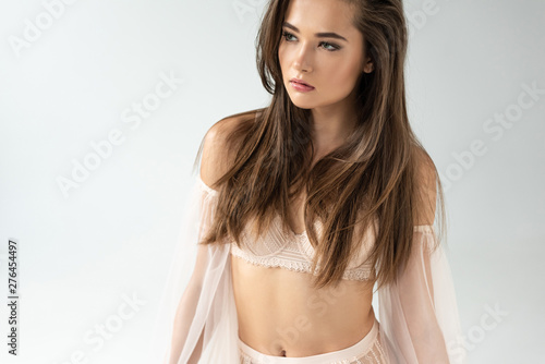 delicate young woman in beige lingerie with mesh sleeves looking away isolated on white