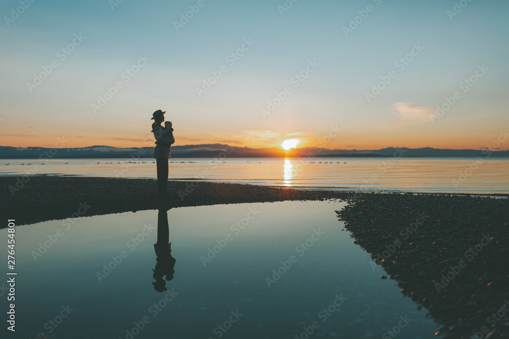 A silhouette of a mother and a baby on the beach at sunset / sunrise.