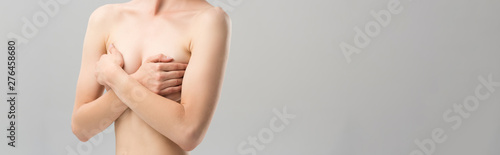 panoramic shot of naked young woman covering breast isolated on grey © LIGHTFIELD STUDIOS