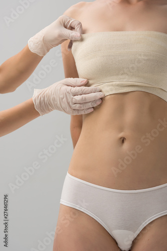 partial view of plastic surgeon in latex gloves and patient in breast bandage isolated on grey © LIGHTFIELD STUDIOS