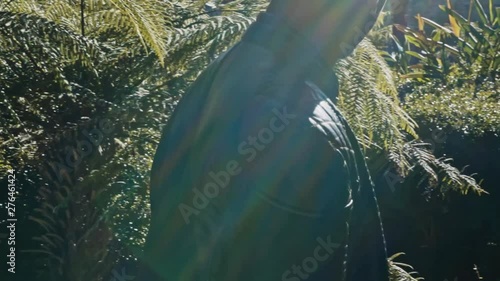 Slow Motion Close Up Of Young Stylish Black Man Walking By Plants in Public Park Under Evening Sunlight With Sun Flares photo