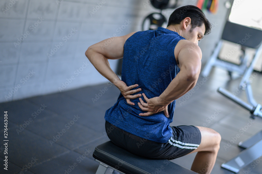 Young man having back pain after workout at the gym. Young man having back pain after workout at the gym.