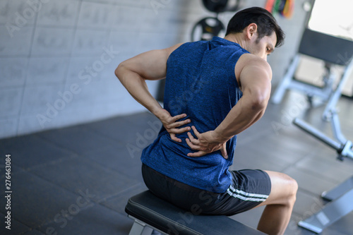 Young man having back pain after workout at the gym.