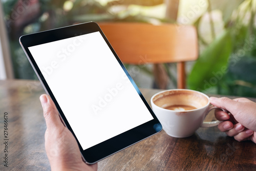 Mockup image of a woman holding black tablet pc with blank white screen and coffee cup to drink