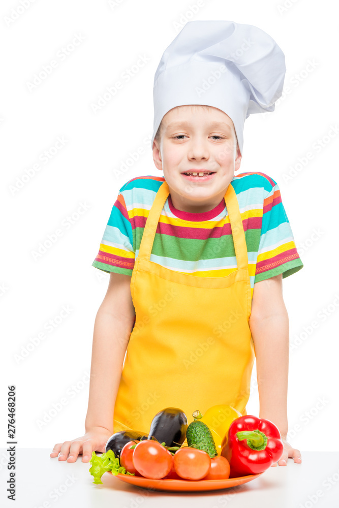 boy in a chef's cap and apron with a plate of vegetables isolated on white background