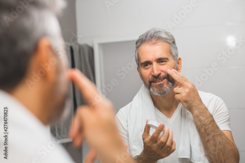 smiling middle aged bearded man applying face cream