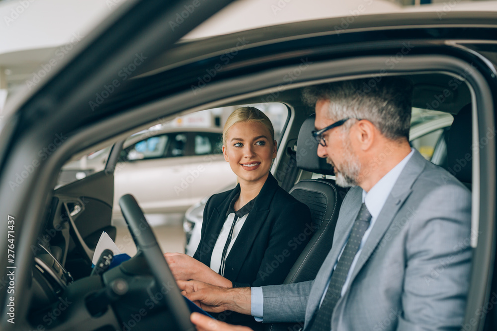 sales woman showing man a new car in car dealership showroom