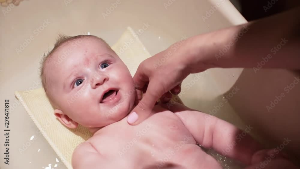 Mother plays with infant baby boy during bathing, he smiles when she tickles him Mother plays with infant baby boy during bathing, he smiles when she tickles him