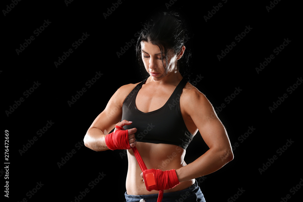 Sporty female boxer applying wrist bands against dark background Sporty female boxer applying wrist bands against dark background