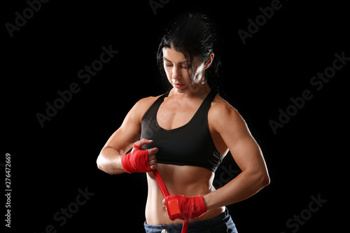 Sporty female boxer applying wrist bands against dark background