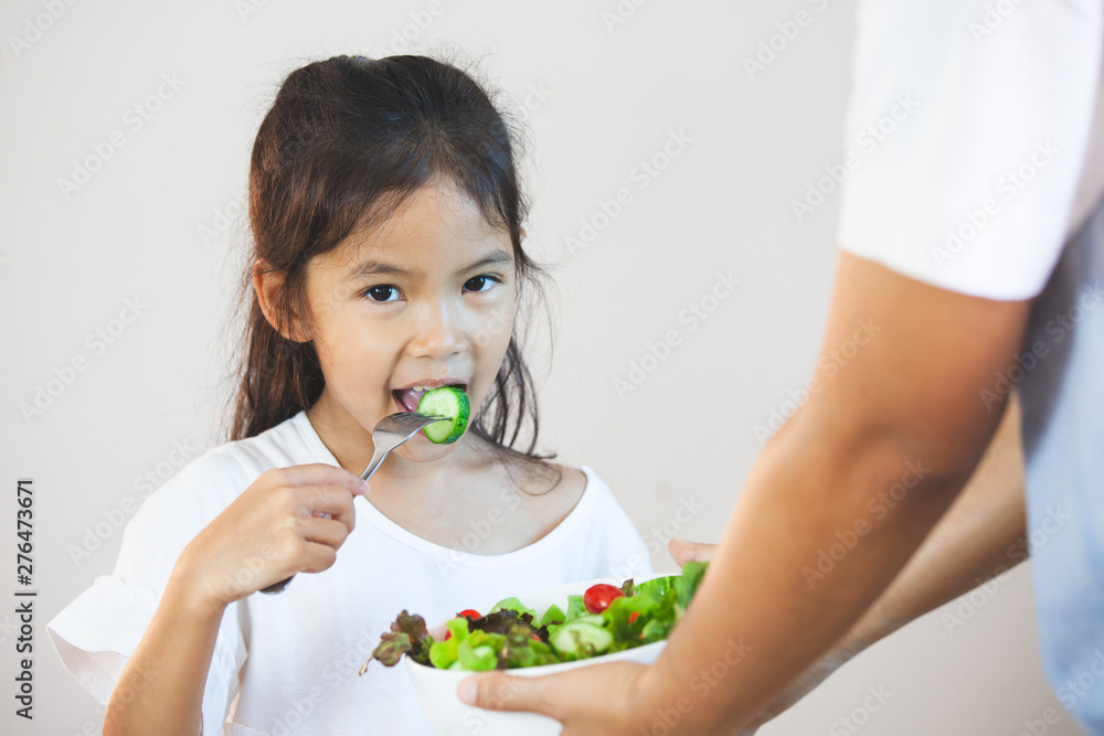Mother give a bowl of salad to asian child girl to eat healthy vegetables for her meal Mother give a bowl of salad to asian child girl to eat healthy vegetables for her meal