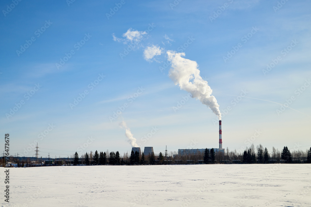 Winter landscape with snowy field and factory with large pipes from which white smoke goes