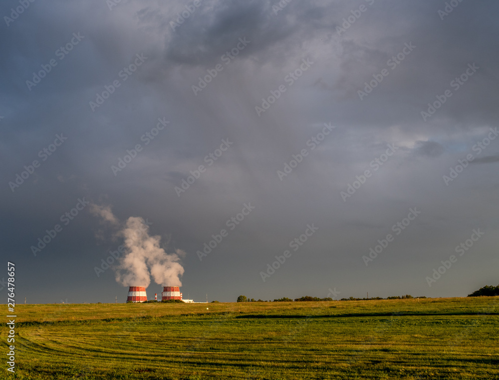 Mown field, grey overcast cloudy sky and steaming cooling towers over horizon Mown field, grey overcast cloudy sky and steaming cooling towers over horizon