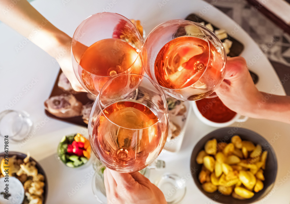 Hands holding glasses with rose wine over the table with food. Hands holding glasses with rose wine over the table with food.