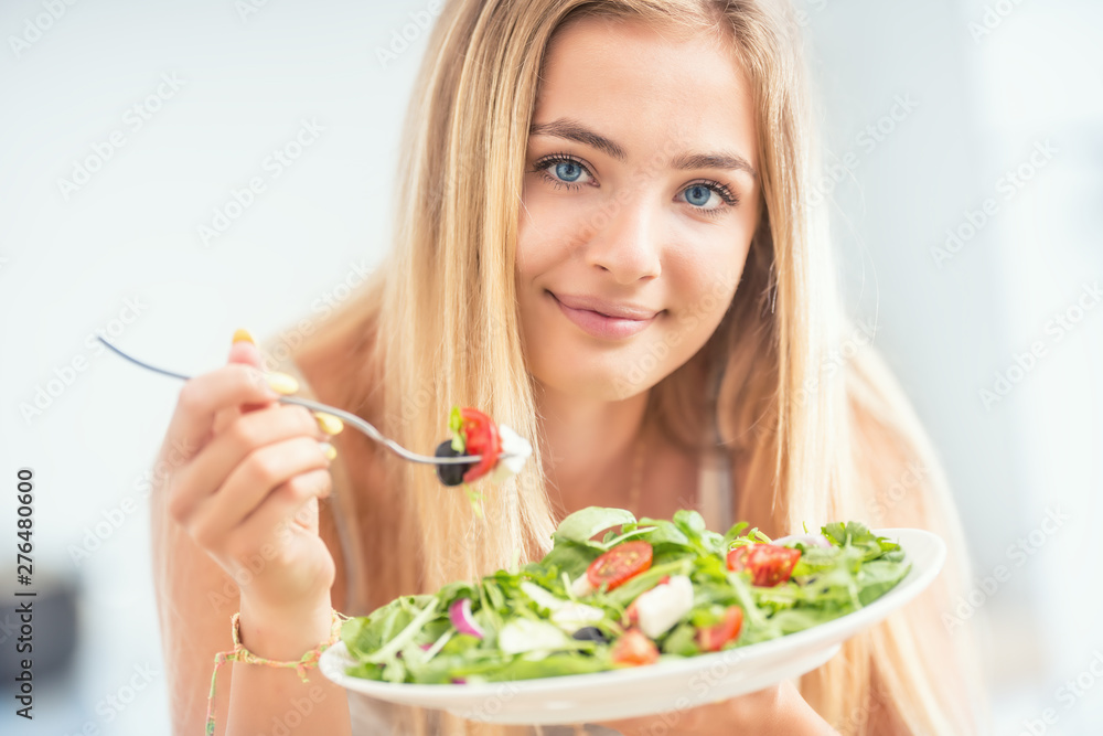 Young happy blonde girl eating healthy salad from arugula spinach tomatoes olives onion and olive oil Young happy blonde girl eating healthy salad from arugula spinach tomatoes olives onion and olive oil