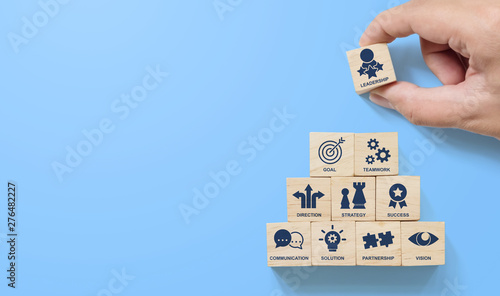 Hand arranging wood block stacking pyramid with icon leader business on blue background. Key success factors for leadership elements concept