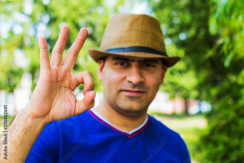 Obraz premium man in hat shows hand gesture OK on nature background